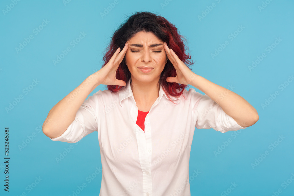 Sudden severe headache. Portrait of distressed fatigued woman employee in shirt rubbing temples, holding head and grimacing in pain, suffering migraine. indoor studio shot isolated on blue background Sudden severe headache. Portrait of distressed fatigued woman employee in shirt rubbing temples, holding head and grimacing in pain, suffering migraine. indoor studio shot isolated on blue background