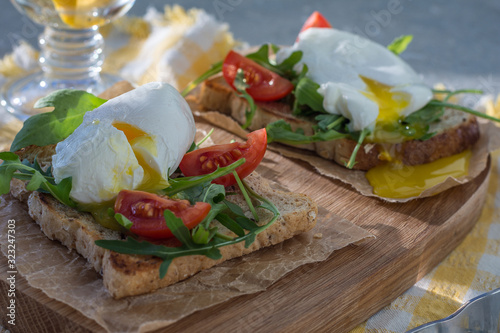 Poached egg on toast with arugula and cherry tomatoes for breakfast on paper and a wooden board horizontal arrangement