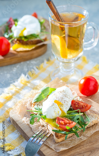 Poached egg on toast with arugula and cherry tomatoes for breakfast on paper and a wooden board with a fork. Vertical arrangement