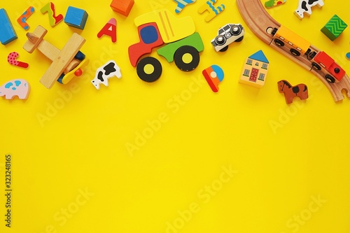 Set of colorful wooden toys for kids, cars, trains, building blocks on yellow background, copy space.