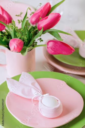 Happy easter. Decor and table setting of the Easter table is a vase with pink tulips and dishes of pink and green color.
