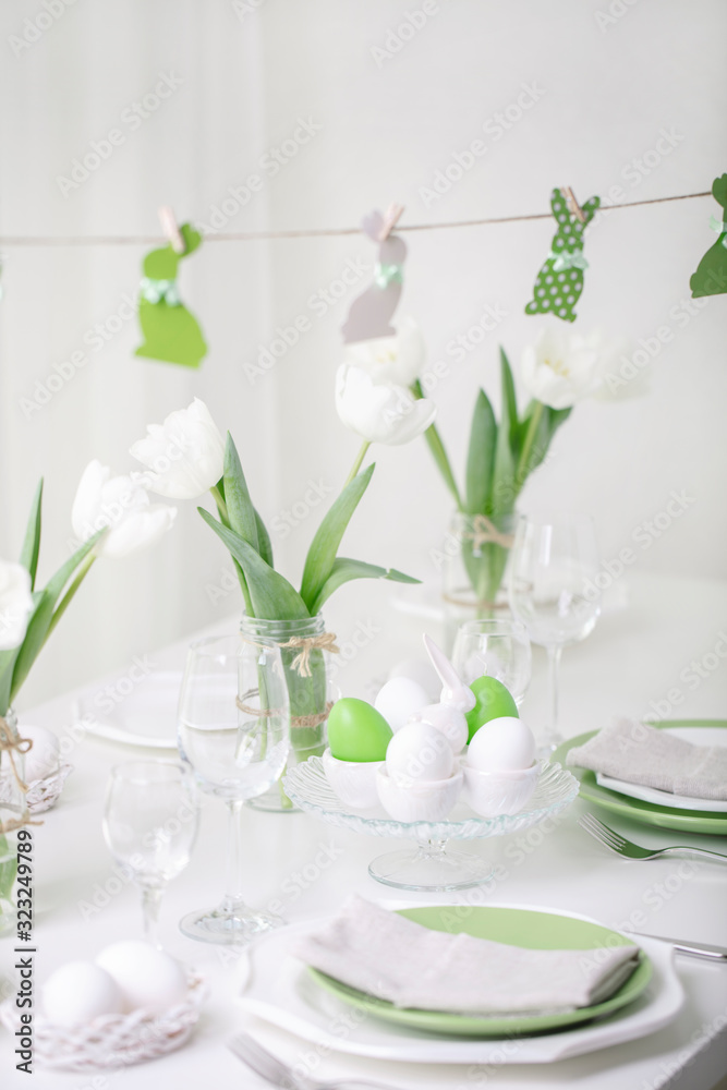 Decor and table setting of the Easter table with white tulips and dishes of green and white color. Easter decor in the form of Easter bunnies green color with white polka dots. Decor and table setting of the Easter table with white tulips and dishes of green and white color. Easter decor in the form of Easter bunnies green color with white polka dots.