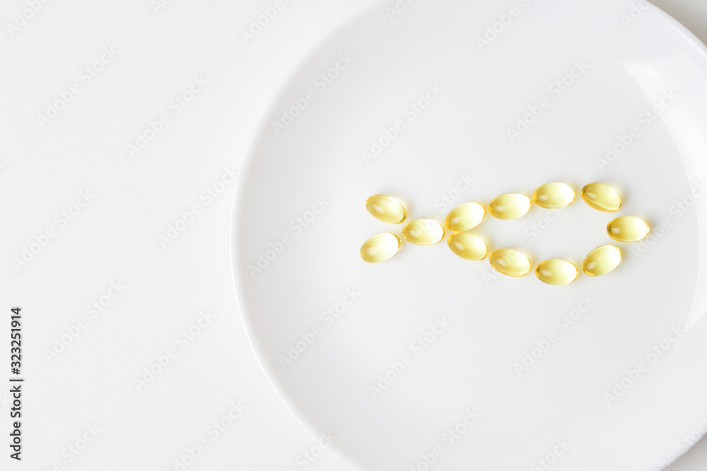 Fish oil softgels on a white plate in a shape of a fish. Meal replacement. Nutrition prescription. Omega-3 polyunsaturated fatty acids. Close-up. Fish oil softgels on a white plate in a shape of a fish. Meal replacement. Nutrition prescription. Omega-3 polyunsaturated fatty acids. Close-up.
