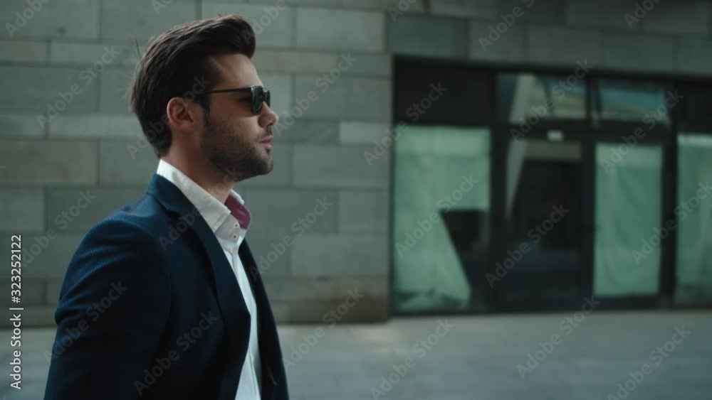 Portrait man wearing sunglasses at street. Man turning head in suit outside