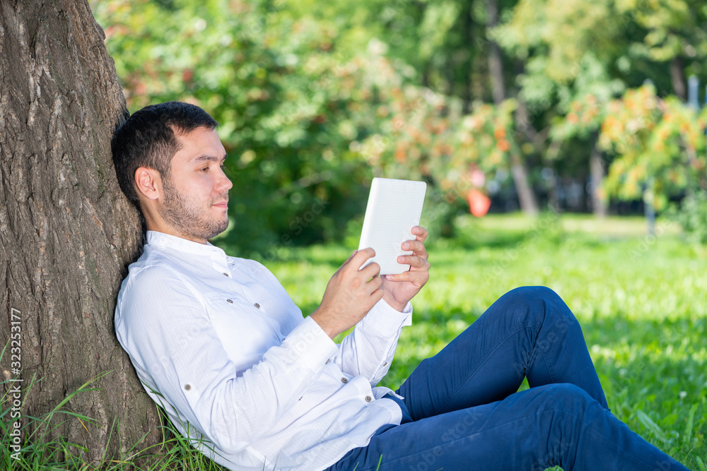 Fototapeta premium Young man using tablet computer under tree