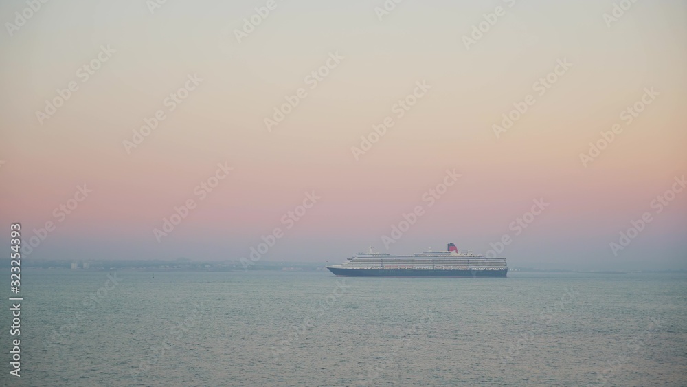 Gimbal shot of a cruise ship on background of pink sunset and horizon. Cruise ship liner goes on the pink horizon sunset line on the blue sea, tourist cruise liner