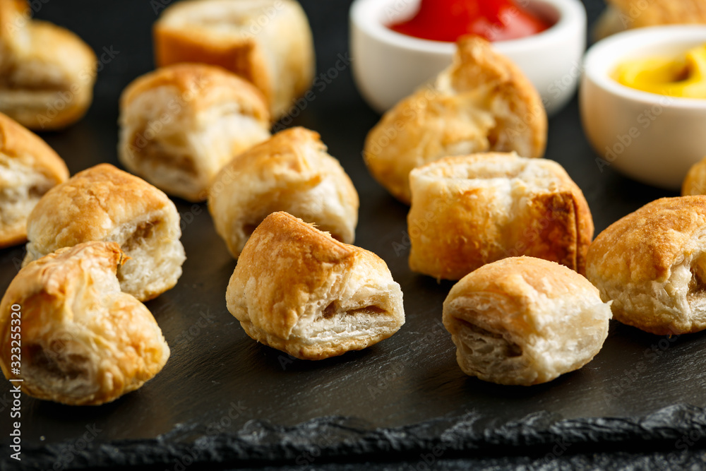 Pork sausage rolls with mustard and ketchup on rustic black stone