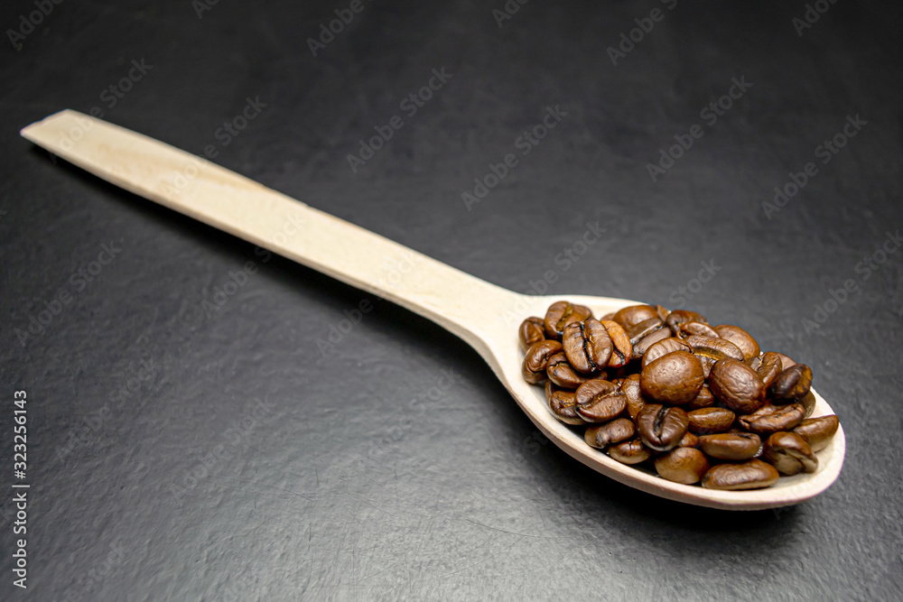 coffee beans on a wooden spoon on a black background coffee beans on a wooden spoon on a black background