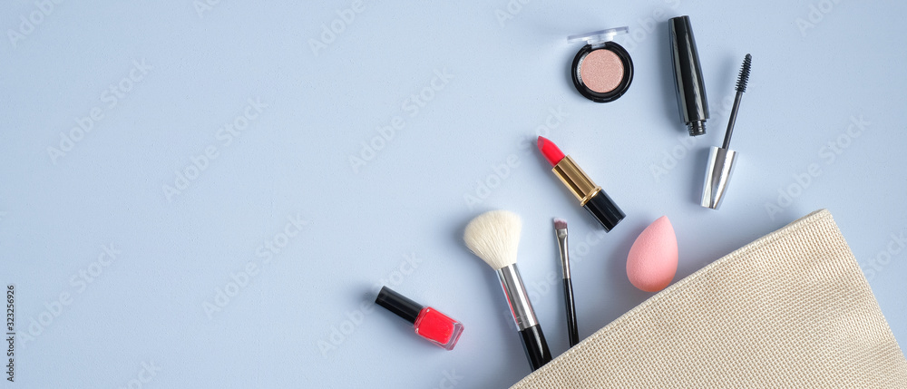 Cosmetic bag and makeup beauty products on blue background with copy space.  Top view make-up brush, lipstick, mascara, eyeshadow spilling out of makeup  artist pouch. Beauty salon banner design foto de Stock