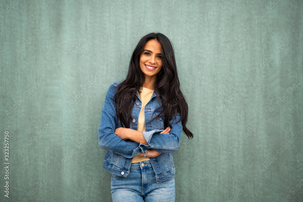 attractive young latin woman smiling by green wall with arms crossed attractive young latin woman smiling by green wall with arms crossed