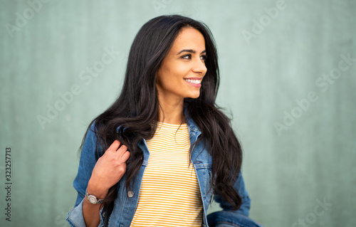 Close up smiling young latin woman looking away by green wall © mimagephotos