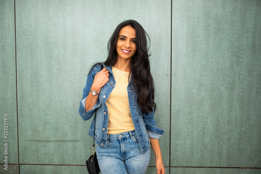 beautiful young arab woman with purse smiling by green wall beautiful young arab woman with purse smiling by green wall