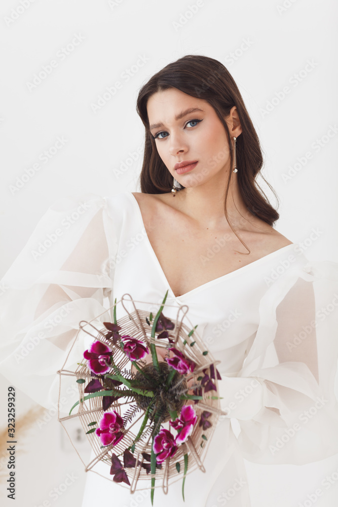 Naklejka premium Portrait of elegant beautiful bride with unusual bouquet of flowers. Perfect makeup and hairstyle