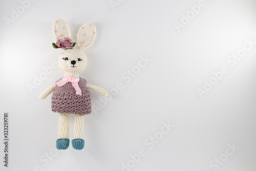 knitted toy rabbit in a sweater-dress with a flower on the ear on a white background