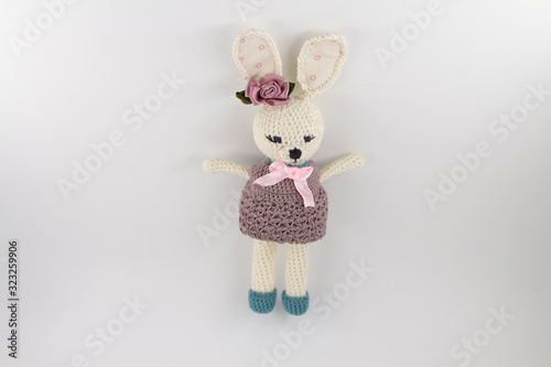knitted toy rabbit in a sweater-dress with a flower on the ear on a white background