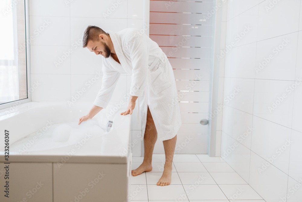 Man in bathrobe fills a bath with water and foam Man in bathrobe fills a bath with water and foam