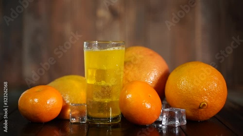 Cold orange drink with ice, oranges and tangerines in a glass glass on a dark background
