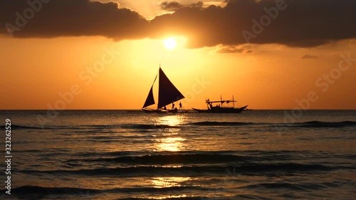 Silhouette Paraw sailing boat and traditional fishing boat crossing each other under orange sunset at Boracay Island of Philippines