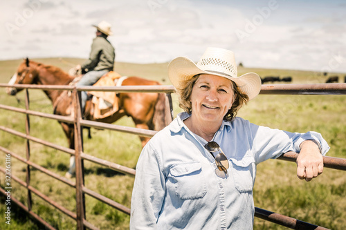 Older Cowgirl leaning on the fence of a branding pen. Cody, Wyoming, USA