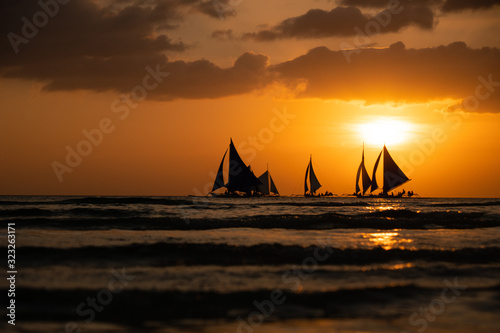 Silhouette Paraw sailing boats under orange sunset at Boracay Island of Philippines