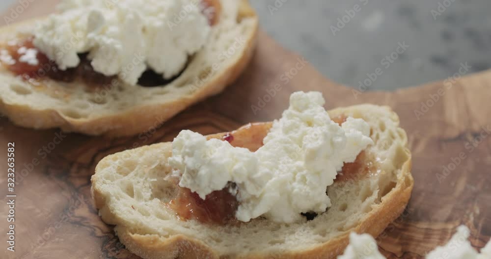 Slow motion handheld shot of bruschetta with ricotta and fig marmalade on olive board