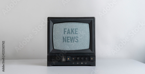 the old vintage tv with gray noise on screen with fake news text overlay, standing on shelf at home photo