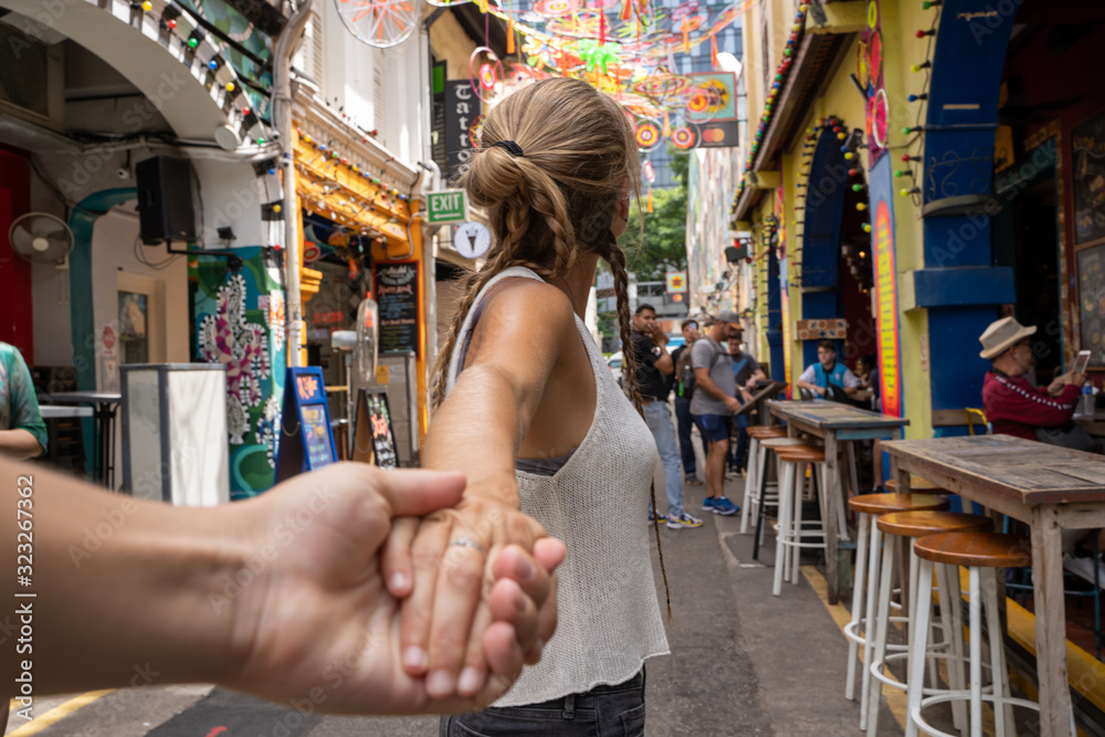 Singapore City, Singapore - 28th January 2020: Girl holding hands with another person on a shopping street with restaurants with colorful facades