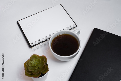 The begining of the work day. Morning at the office. Student workplace. A cup of coffee, a black notebook, a white sheet with an empty place for text and a plant on a white background. View from abov photo