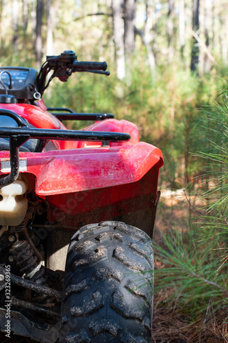 Fényképezés Red four wheeled ATV close up in the forest with a pine tree background ~DIRT~