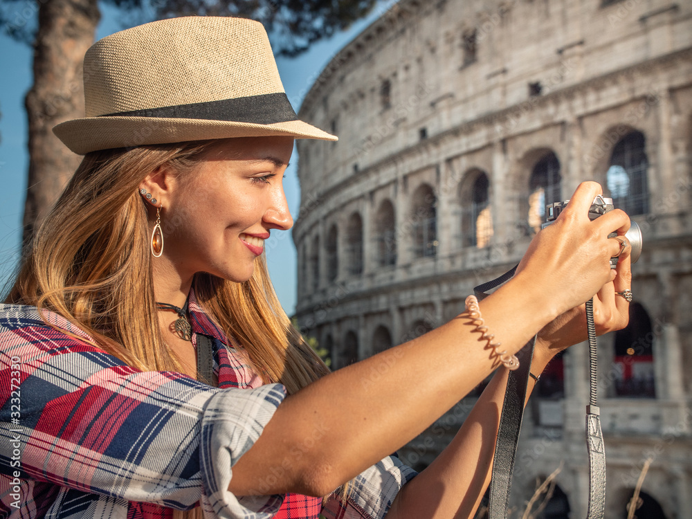 Ταπετσαρία Young blonde woman with blue eyes and long hair, taking pictures with a vintage camera at Colosseum, Rome