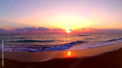 Ocean waves crashing on sand beach in stunning orange colored warm evening sunset at seaside landscape in steady view