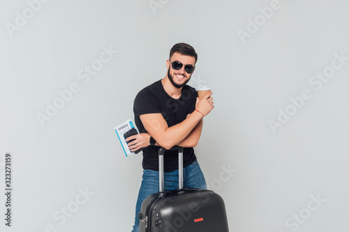 Portrait of young businessman, tourist with a passport and suitcase and  phone isolated on white background. Holding cup with coffee.
