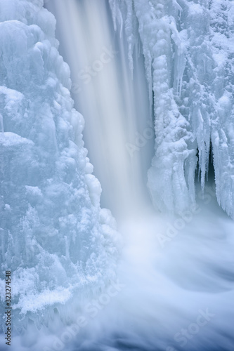 Winter landscape of the Comstock Creek cascade framed by ice and captured with motion blur, Michigan, USA