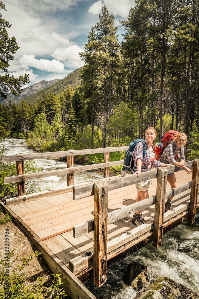Two girlfriends taking a break on a bridge while hiking in the mountains. Red Lodge, Montana, USA Two girlfriends taking a break on a bridge while hiking in the mountains. Red Lodge, Montana, USA