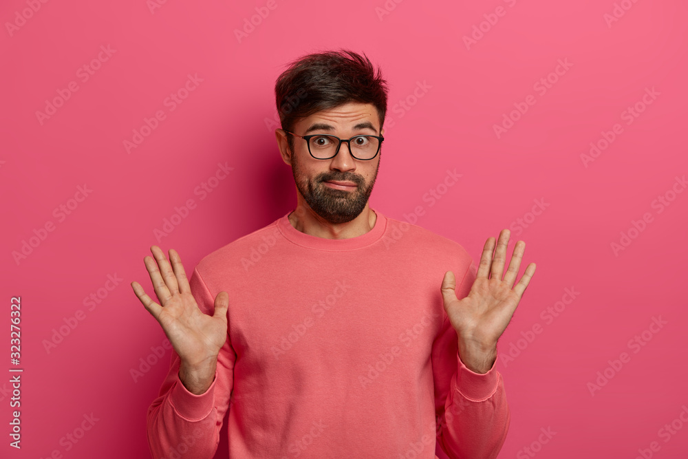 Naklejka premium Portrait of bearded man raises palms, shows beig not involved or guilty, gestures in studio, has confused look after doing something wrong, feels sorry, wears pink jumper. I couldnt handle it