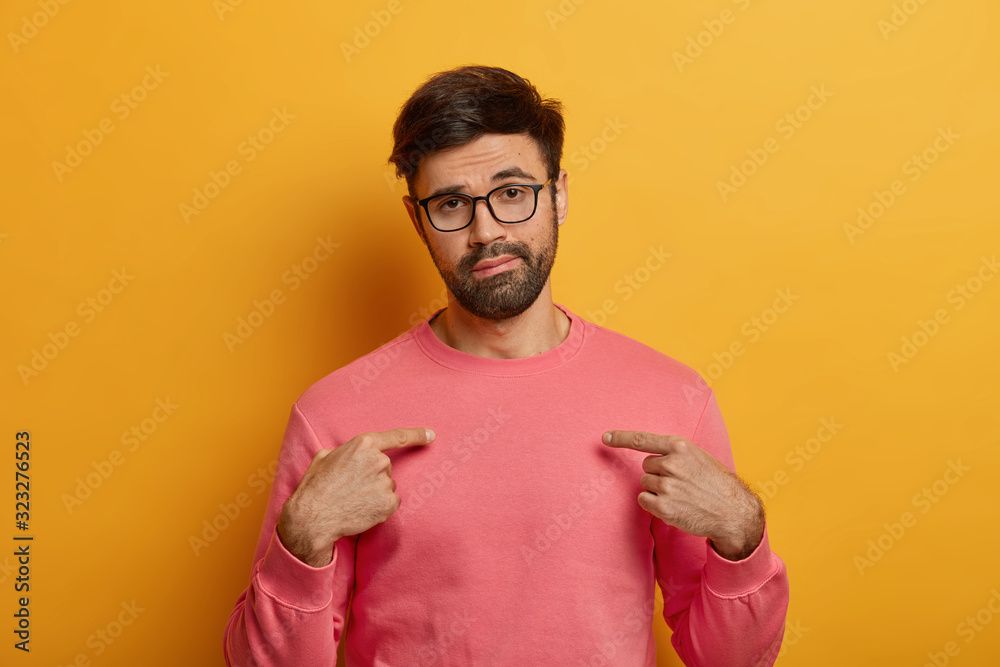 Unimpressed tired man points at himeself, shows his new pink jumper, wears glasses, advertises clothes, looks unwillingly at camera, isolated over yellow background. Copy space for your design Unimpressed tired man points at himeself, shows his new pink jumper, wears glasses, advertises clothes, looks unwillingly at camera, isolated over yellow background. Copy space for your design