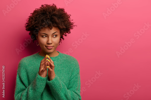 Фотография Serious curly haired woman steepls fingers, has cunninng expression, says everyt