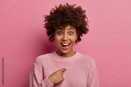 Happy questioned woman has unbelievable expression, points at herself and makes sure she heard right, surprised and glad being chosen to participate in interesting event, asks who me really?