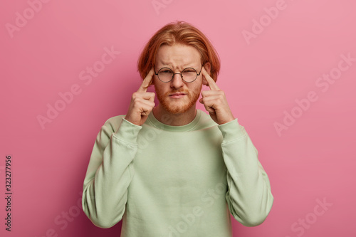 Foto Intense bearded man touches temples with both index fingers, has dissatisfied fa
