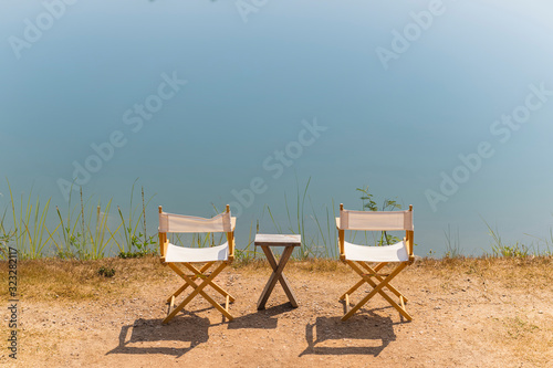 Fototapeta Naklejka Na Ścianę i Meble -  Empty two wooden chair and wooden table in the sun and near river