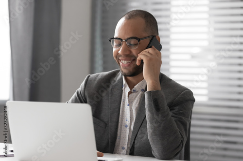 Smiling male employee working on laptop talking on cell