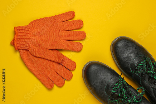 Leather work boots and gloves on yellow background. Worker safety. Top view photo