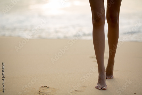 beautiful tanned legs of the girl go next to the sea and footprints in the sand