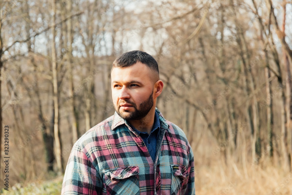 Bearded hipster man with serious face is thinking about something while standing outdoors against autumn fall with copy space, stylish brutal male with trendy look walking in park at sunset. Bearded hipster man with serious face is thinking about something while standing outdoors against autumn fall with copy space, stylish brutal male with trendy look walking in park at sunset.