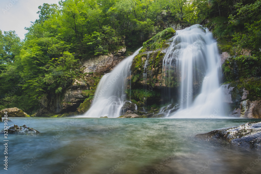 Fototapeta premium Long exposure of magical looking Virje waterfall in Slovenia, close to bovec. Dreamy and enchanting water falling down the cliff above the small alpine lake.