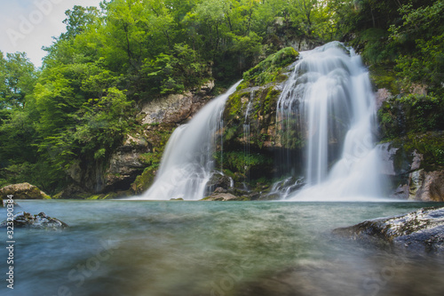 Long exposure of magical looking Virje waterfall in Slovenia, close to bovec. Dreamy and enchanting water falling down the cliff above the small alpine lake.