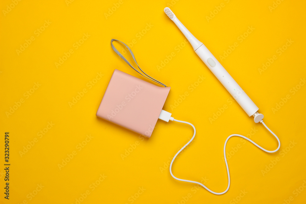 Modern electric toothbrush charging with power bank on yellow background. Top view