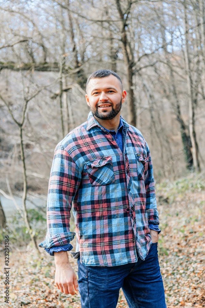 Bearded hipster man with serious face is thinking about something while standing outdoors against autumn fall with copy space, stylish brutal male with trendy look walking in park at sunset.