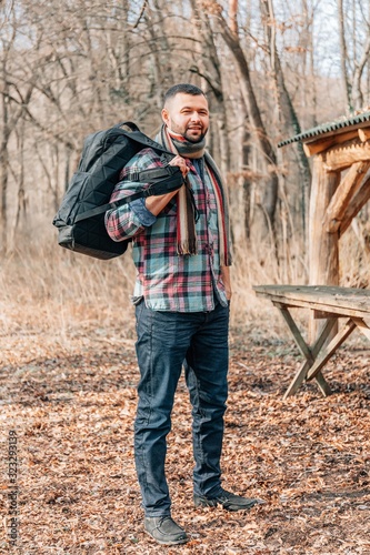 Male tourist exploring new places. Handsome man travel on autumn forest sitting on table near lake. Young bearded man travels with a backpack on a autumn day outdoors.