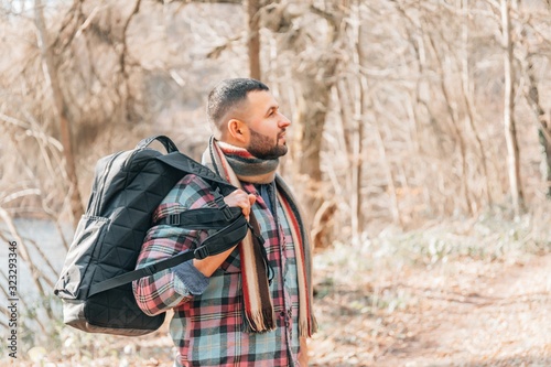 Male tourist exploring new places. Handsome man travel on autumn forest sitting on table near lake. Young bearded man travels with a backpack on a autumn day outdoors.